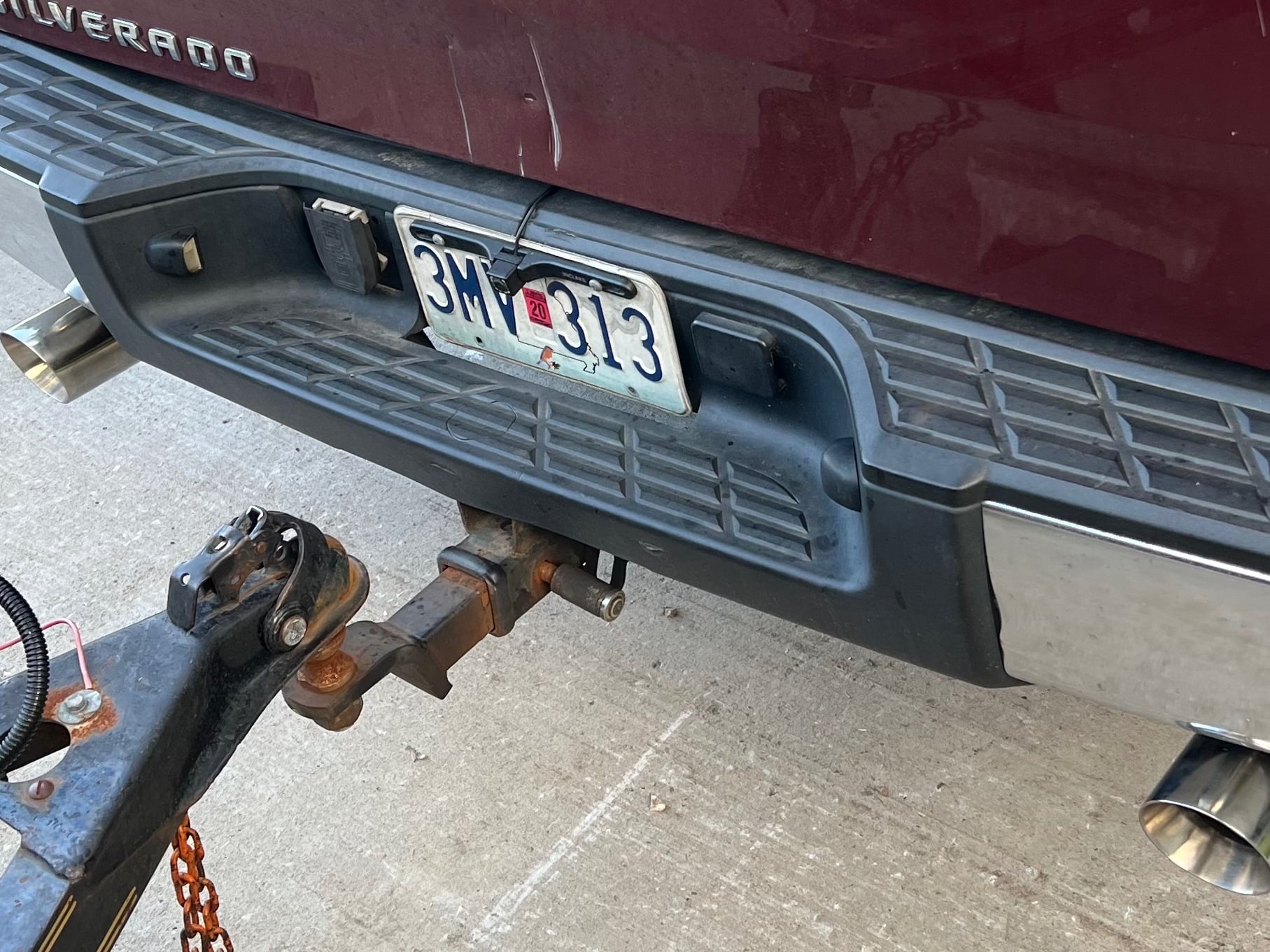 Rear view of a Chevrolet Silverado towing setup, showing a trailer hitch receiver, polished dual exhaust tips, and a cat-back exhaust system with ample clearance around the hitch for towing.