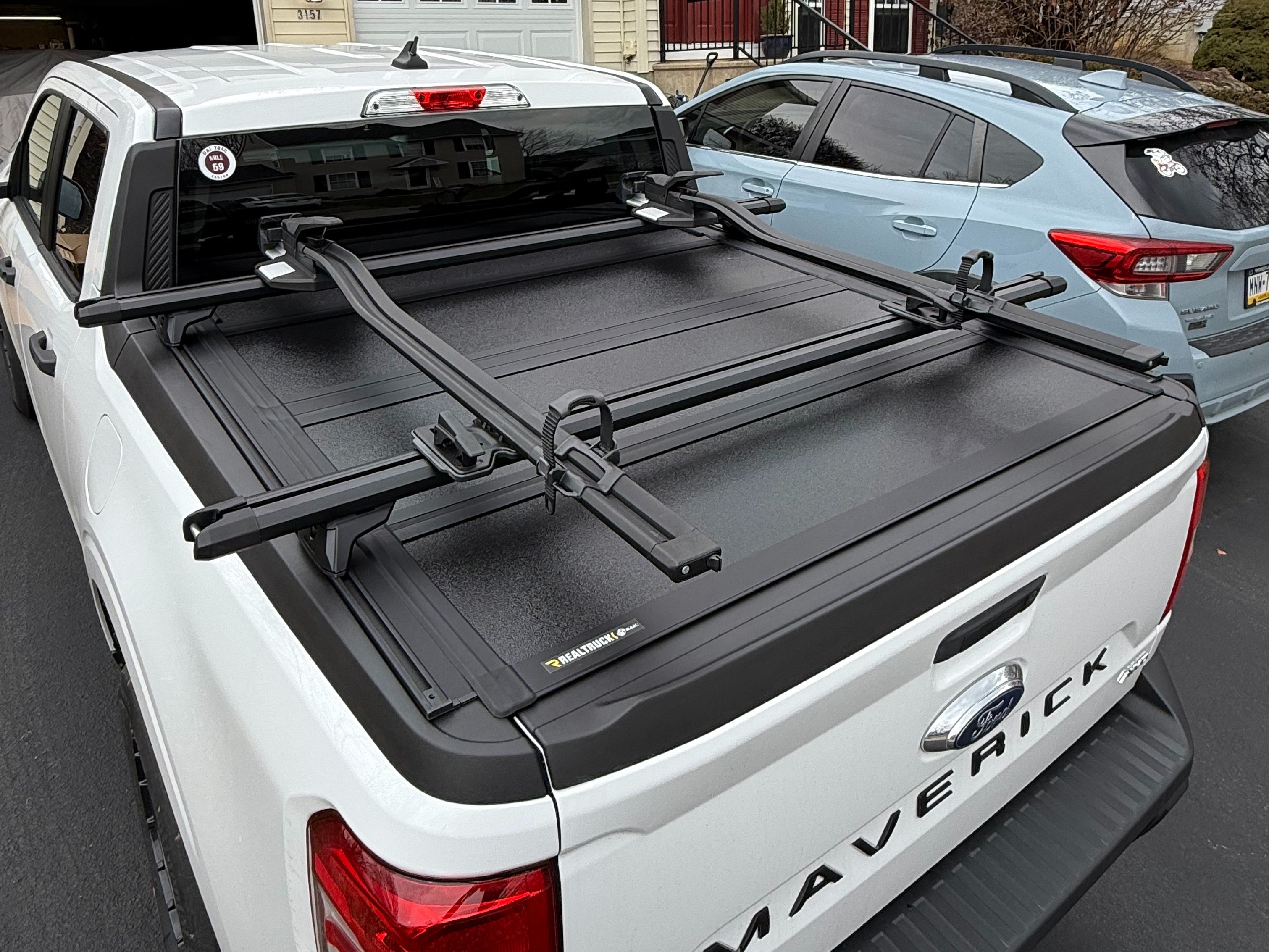White Ford Maverick with a retractable tonneau cover and adjustable bed rack system, featuring crossbars mounted above the truck bed for transporting bikes, kayaks, ladders, or other oversized cargo while keeping the bed covered.