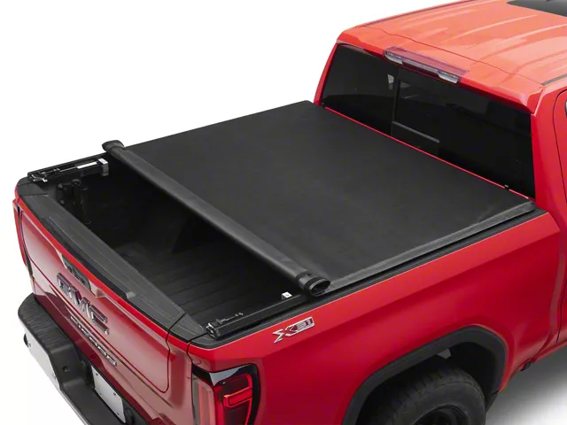 Red GMC Sierra with a TruXedo TruXport soft roll-up tonneau cover partially rolled open, providing quick access to the front of the truck bed while keeping the rear cargo area covered.