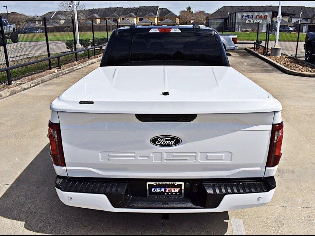 White Ford F-150 with a painted one-piece hinged tonneau cover closed over the truck bed, providing a flush, color-matched appearance and weather-resistant cargo protection.