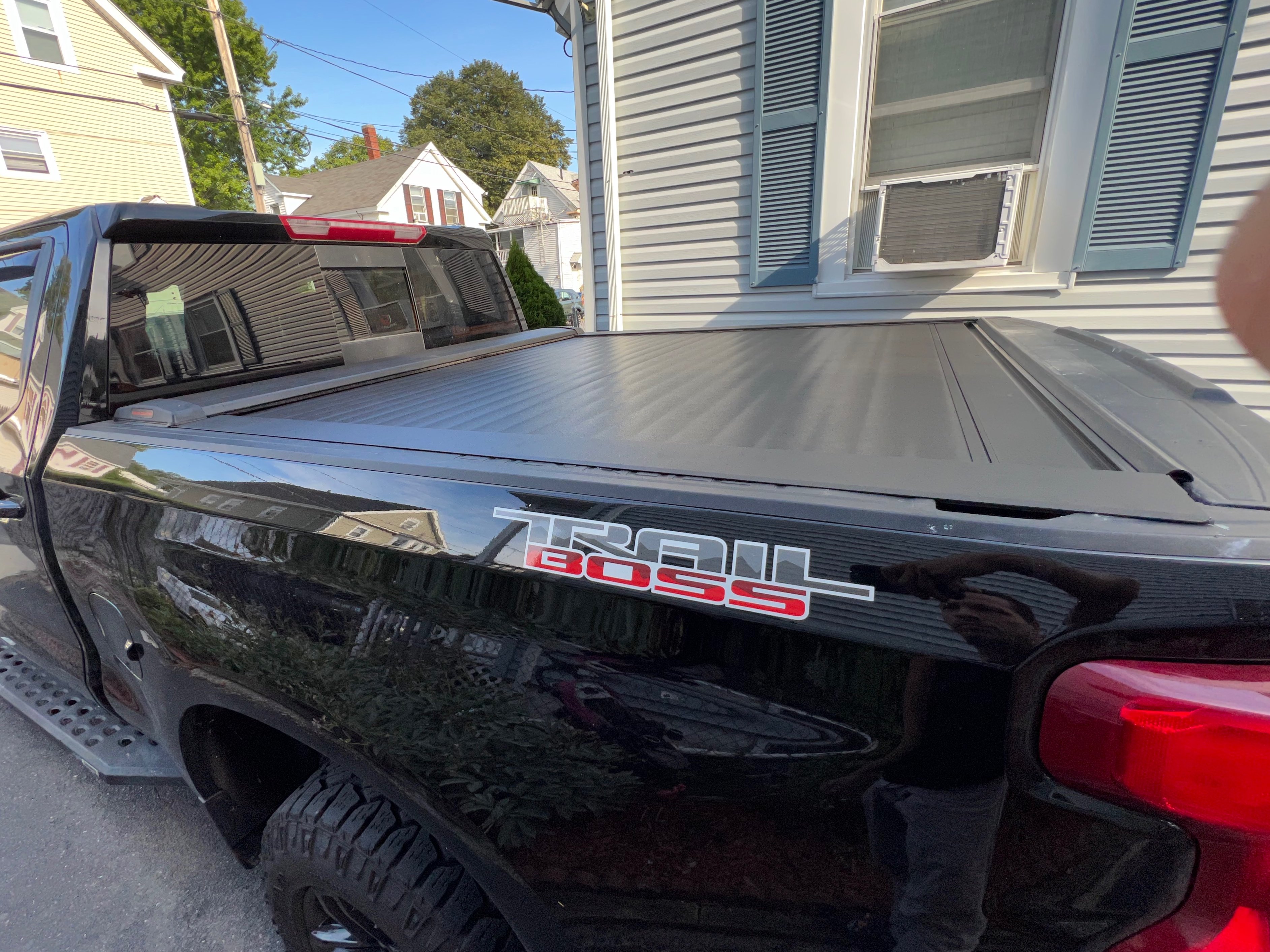 Black Toyota Tacoma with a retractable aluminum tonneau cover closed over the truck bed, featuring a low-profile design that slides into a front canister for secure cargo protection.