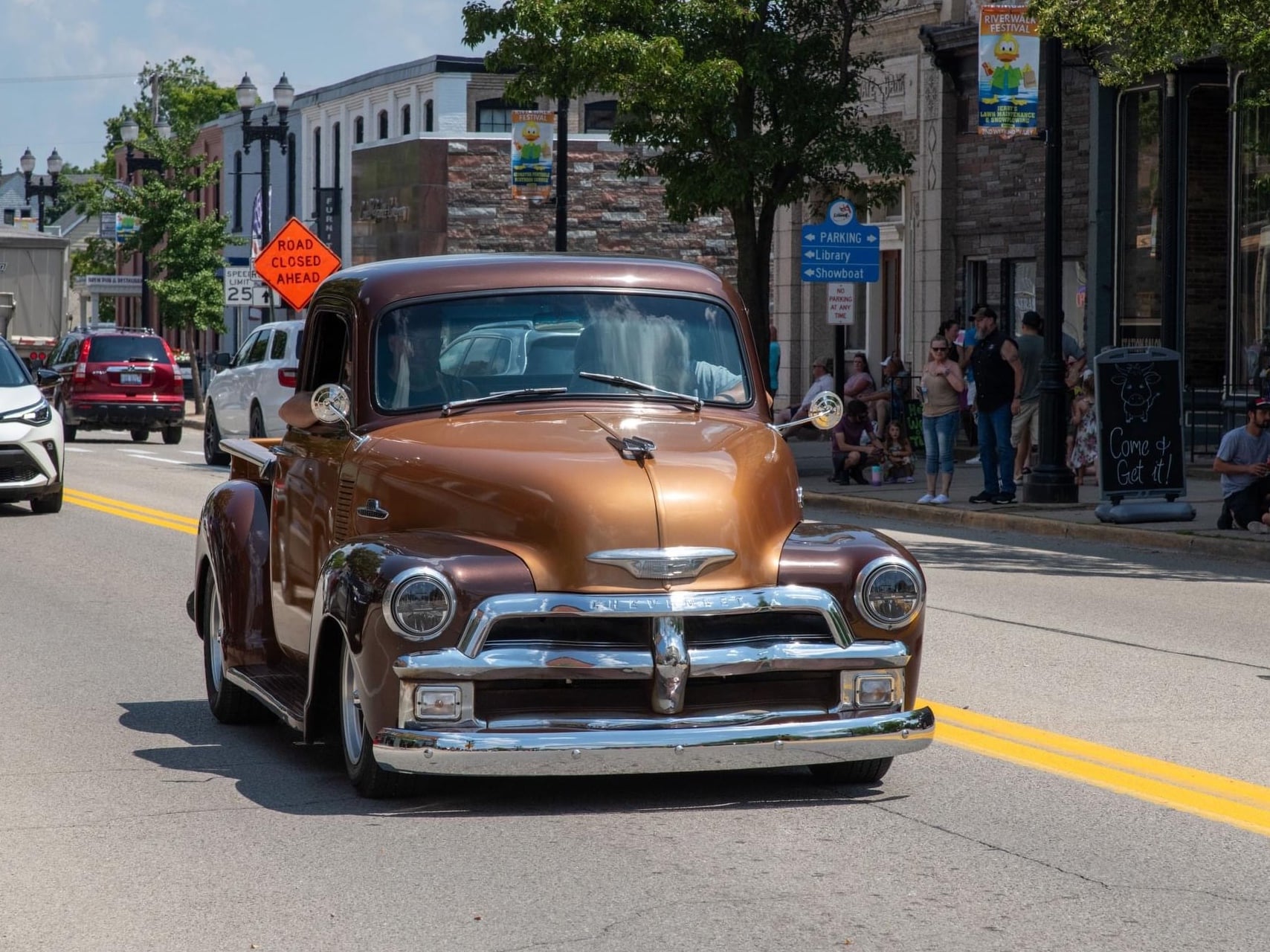 Classic brown Chevrolet pickup truck driving down a city street during a parade.