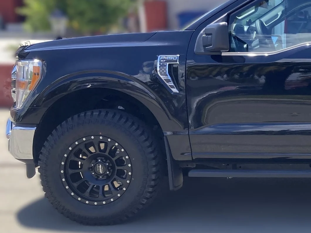 Black Ford F-150 with aftermarket black beadlock-style wheels and all-terrain tires, illustrating a common six-lug wheel setup for full-size pickup trucks.