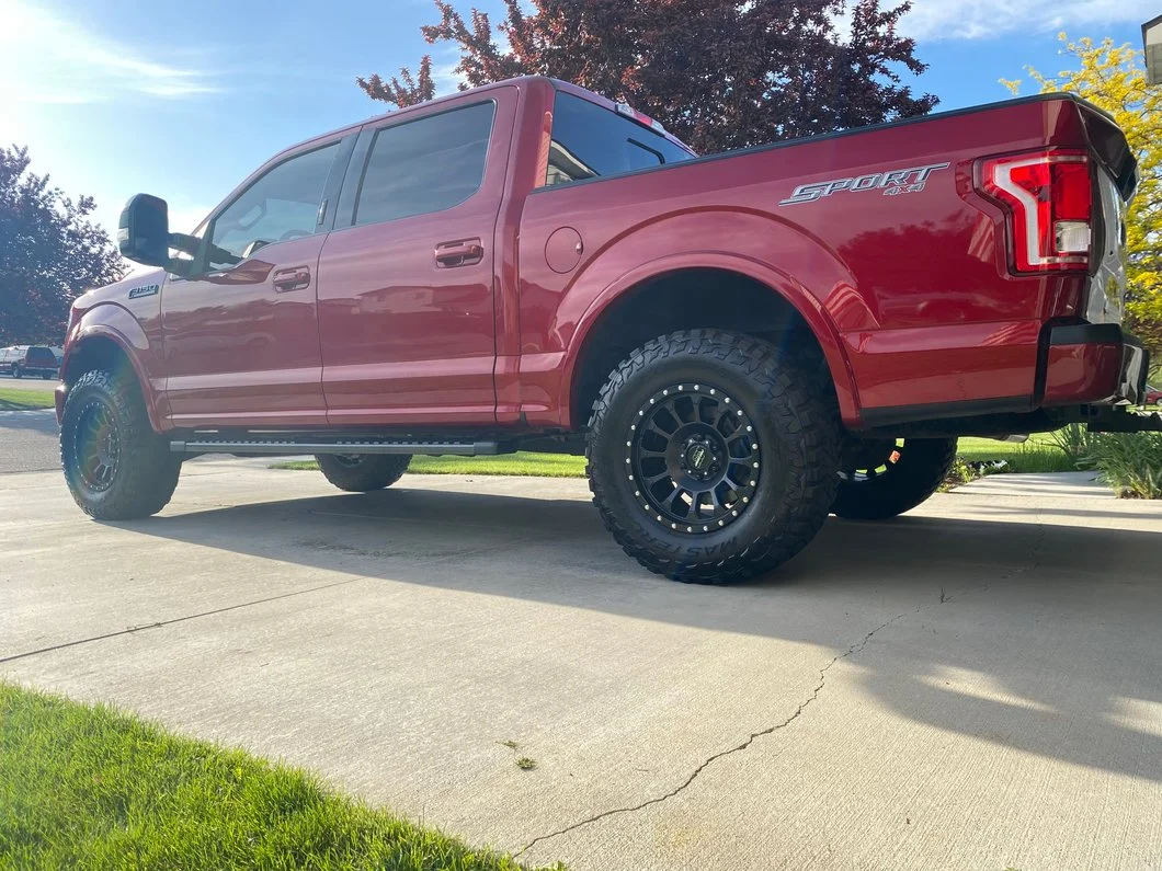 Red Ford F-150 with a suspension lift, aftermarket black wheels, and all-terrain tires, demonstrating a lifted truck with a six-lug wheel setup.