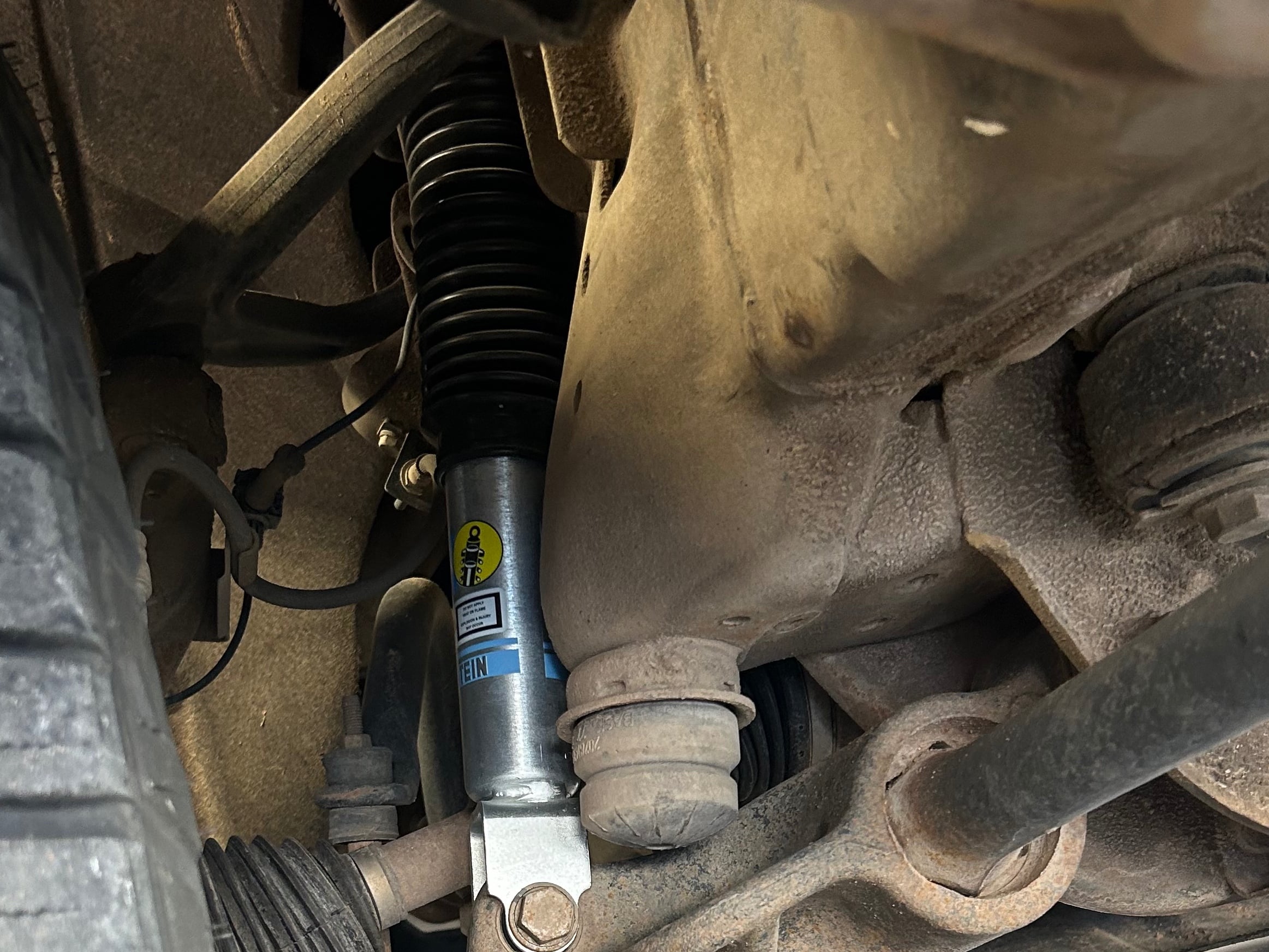 Bilstein monotube shock absorber installed on a pickup truck's front suspension, mounted between the control arm and frame to improve ride control, handling, and towing performance.