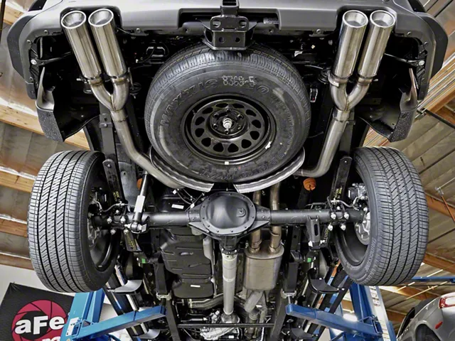Underside view of a pickup truck with a dual-exit performance exhaust system, showing stainless steel exhaust tubing, quad exhaust tips, and the rear axle mounted on a vehicle lift.